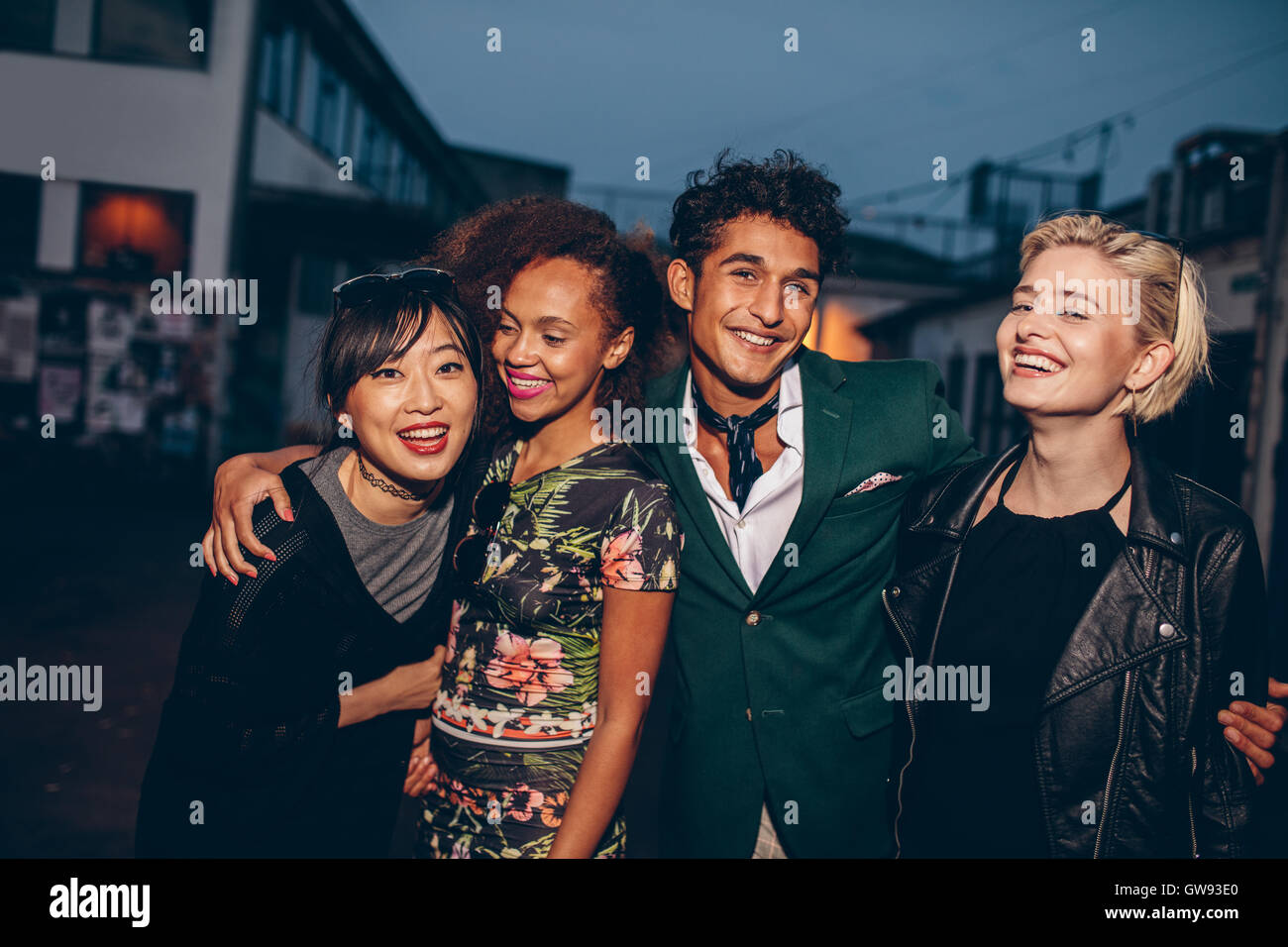 Group of friends walking on city street together at night. Multiracial young man and women enjoying outdoors in evening. Stock Photo