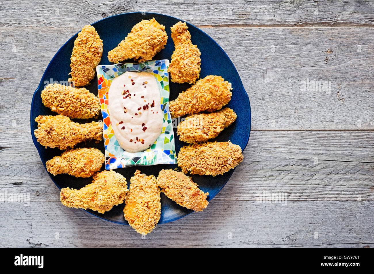 Top view of homemade baked crispy chicken wings on a blue ceramic plate with creamy yogurt garlic and chili flake dip Stock Photo