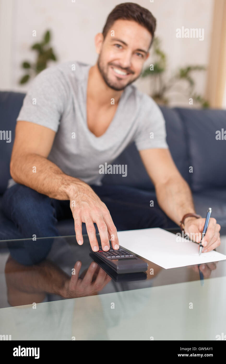 Happy man calculating indoor, writing on blank paper with pen, using calculator. Stock Photo