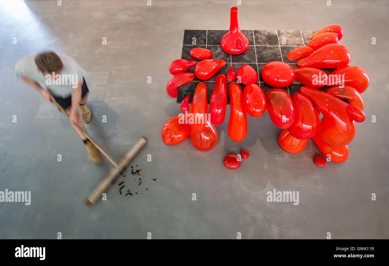 A technicians sweeps the floor next to Vulcano Table, 2014 (Blown glass, Ferrari red pigment, limestone tiles, powder coated metal) by Turner Prize nominee Anthea Hamilton, as he puts the finishing touches to the Kettle's Yard Reimagined: Anthea Hamilton exhibition, showing at The Hepworth Wakefield from September 15 2016 until March 19 2017. Stock Photo