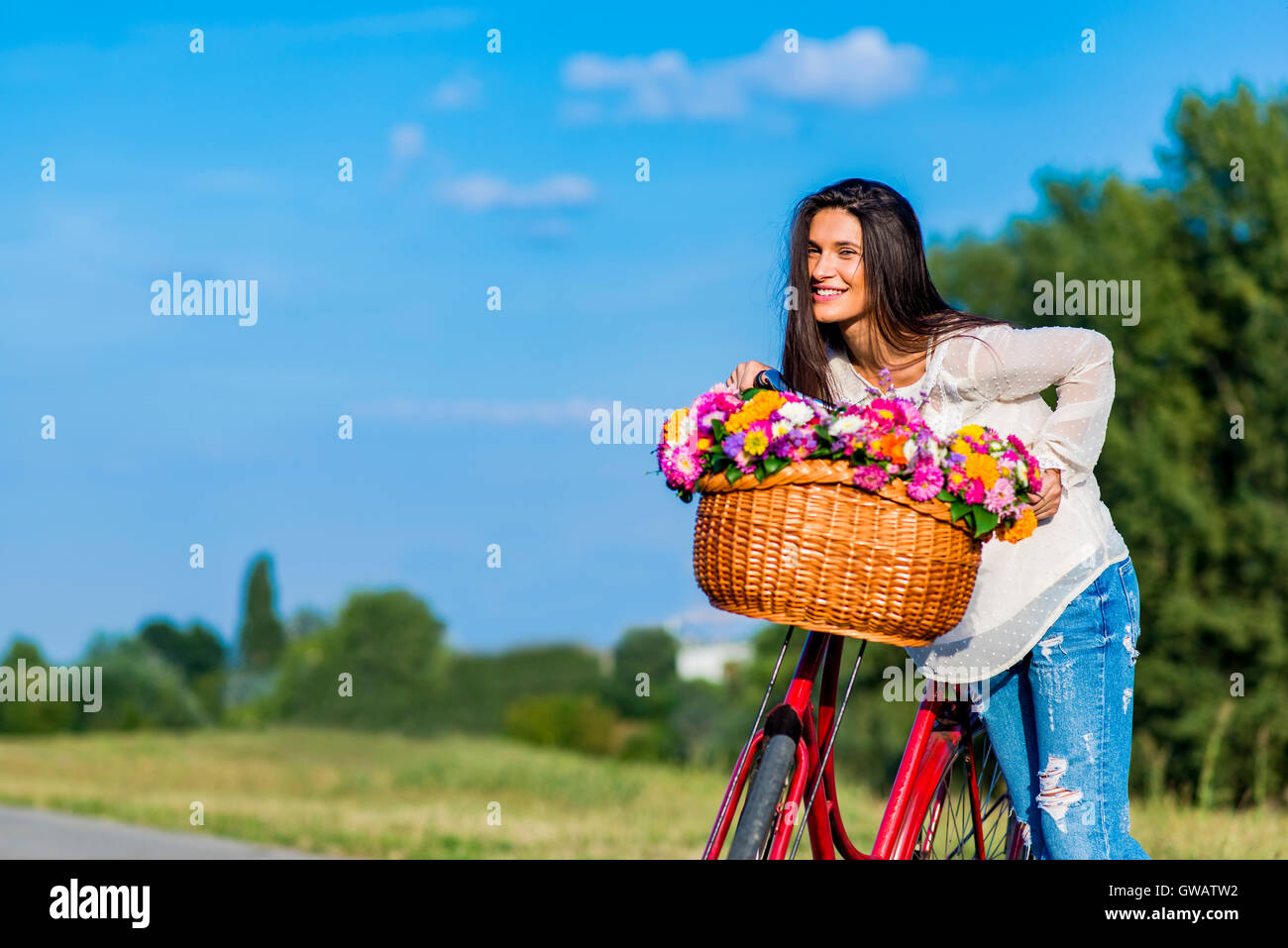 Young girl posing by a bicycle with a basket full of flowers Stock Photo