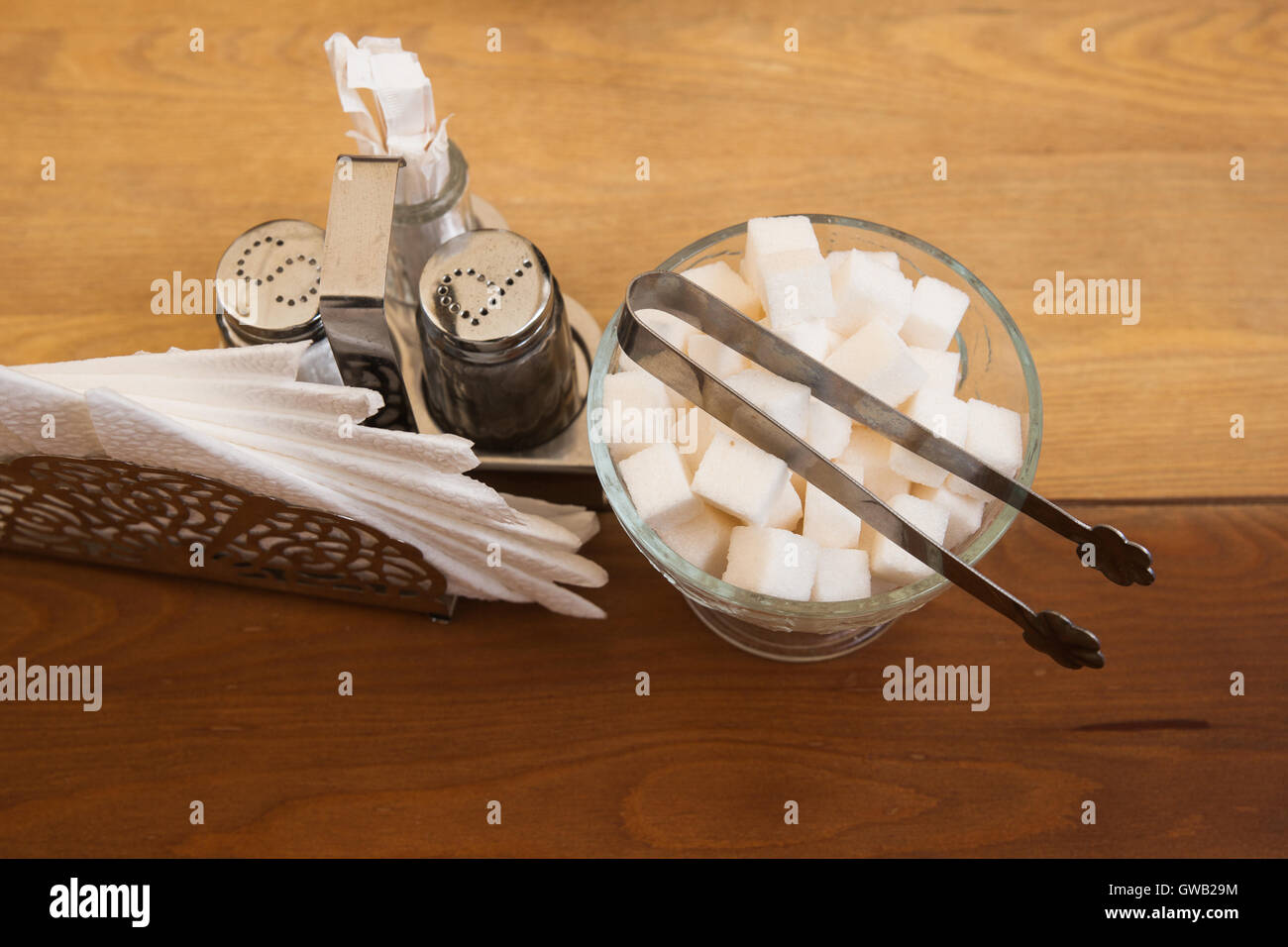 Brown color table with cube sugar bowl. White napkins, salt and pepper set, sugar tongs. Stock Photo