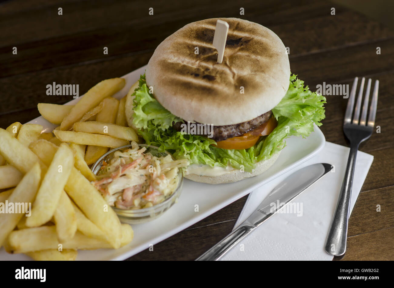 a beef burger served on a rectangular plate with chips and coleslaw, on
