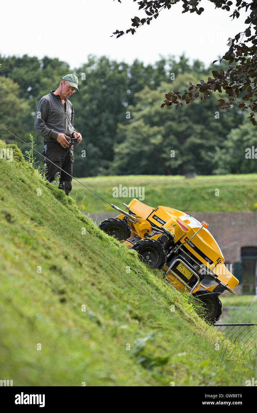 A remote control industrial grass cutter on a steep sloping city wall of the city of Naarden vesting. Stock Photo