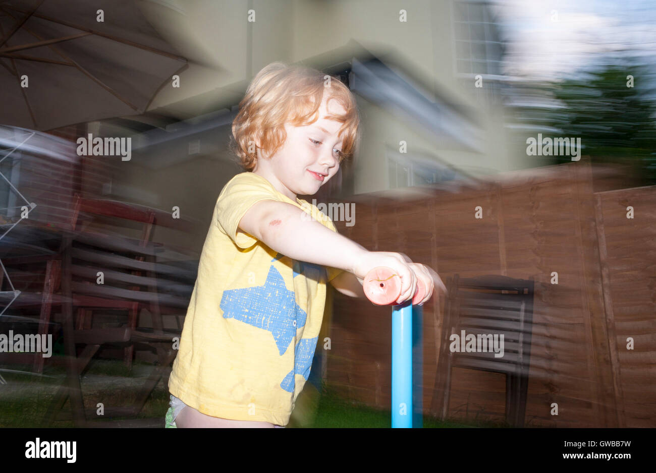 Image of a young 3-year old boy using a scooter in the garden using slow-sync flash technique Stock Photo