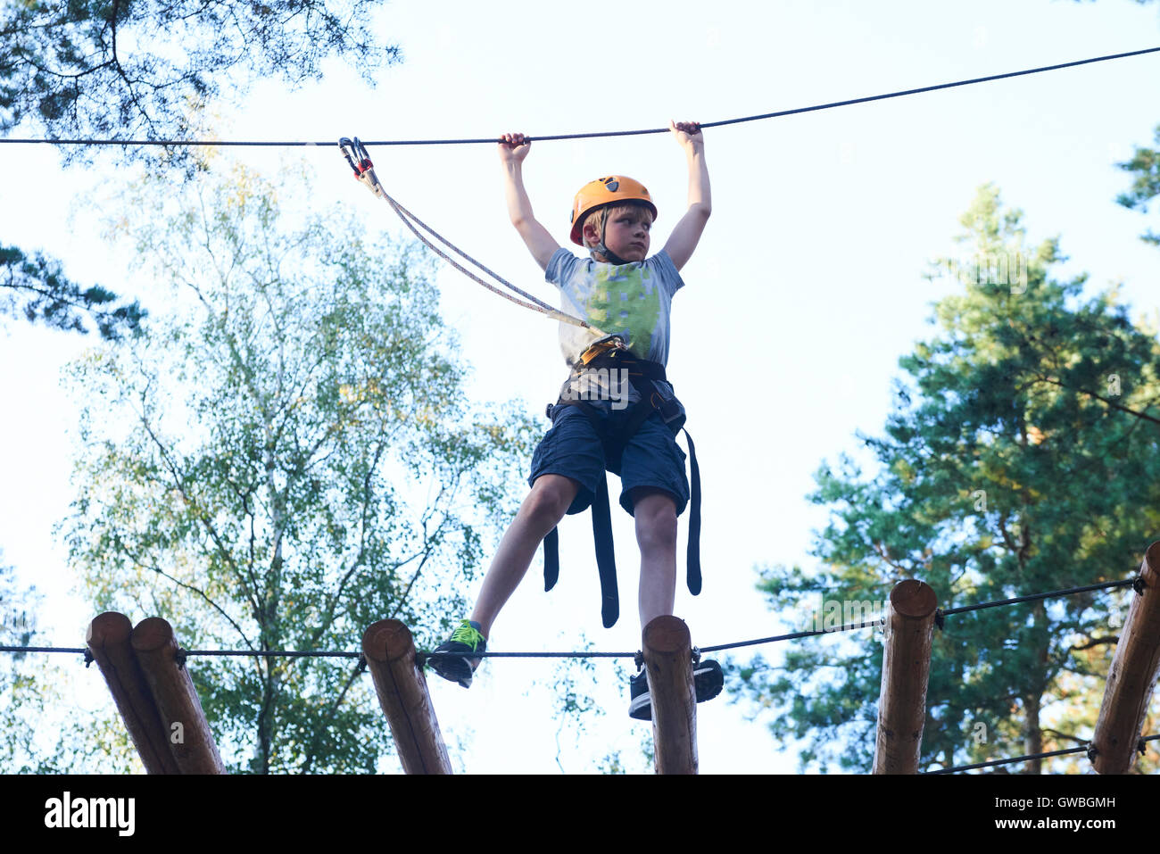 Portrait of active brave boy enjoying outbound climbing at adventure park on tree top Stock Photo