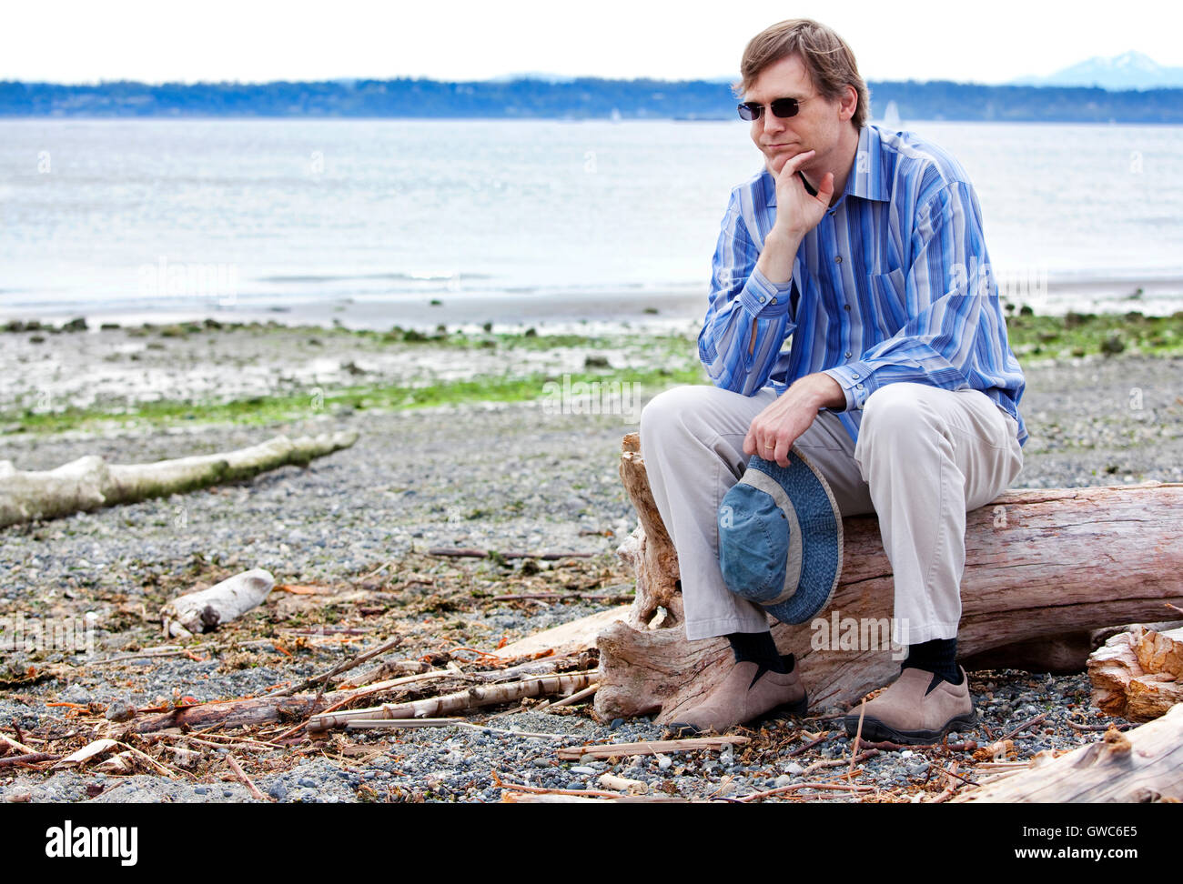 Depressed man sitting on driftwood on beach Stock Photo