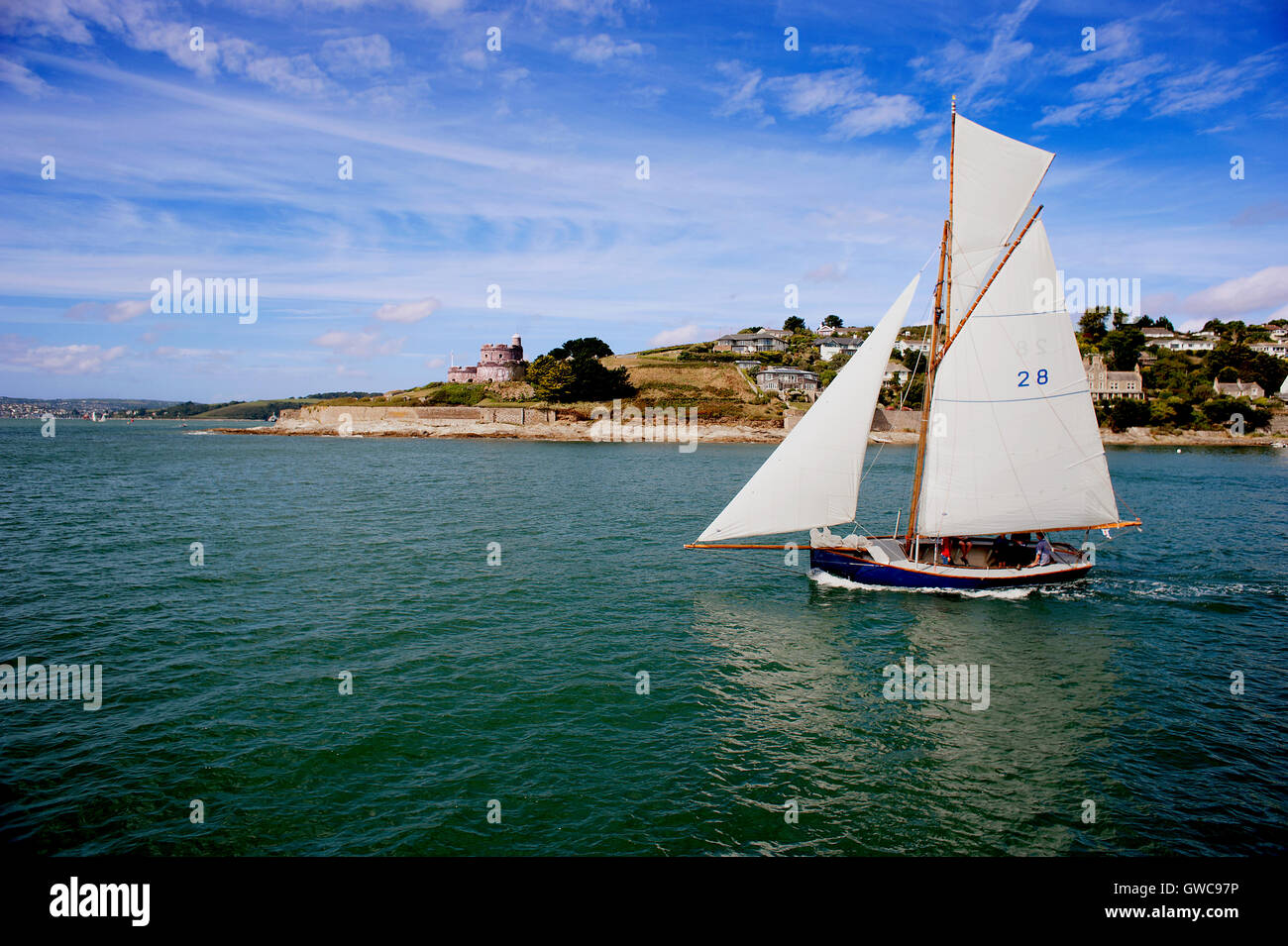 A yacht sails out of St Mawes harbour past the castle built by Henry VIII on a beautiful English summer's day in Cornwall. Stock Photo