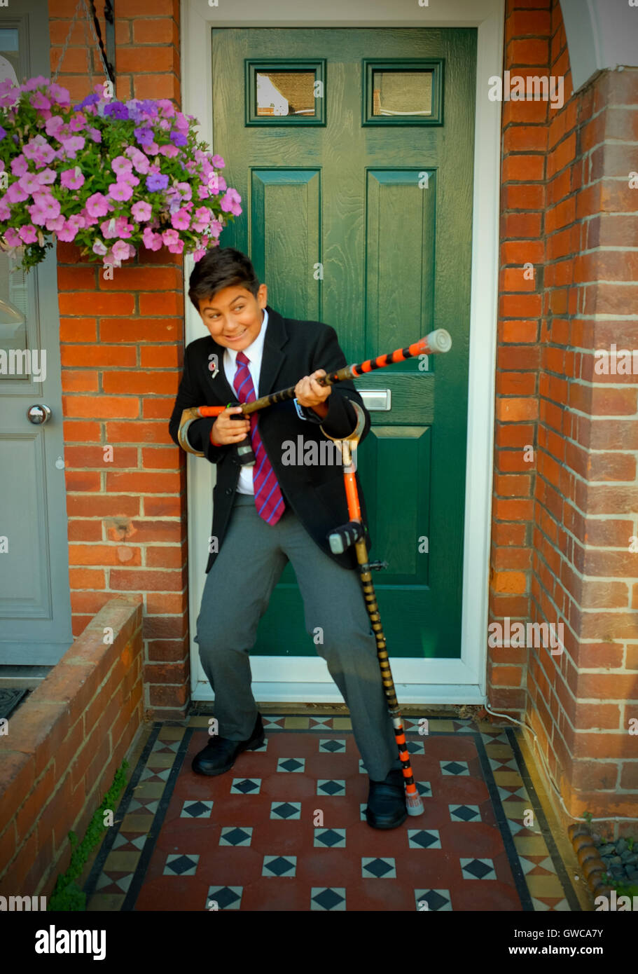 12 year old school boy in school uniform outside the front door of his house, he has crutches and is pointing one of them Stock Photo