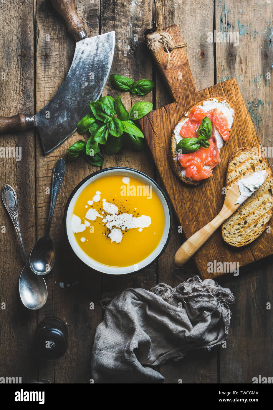 Dinner or lunch with pumpkin cream soup and salmon, ricotta and basil toasts over old rustic wooden background, top view, vertic Stock Photo