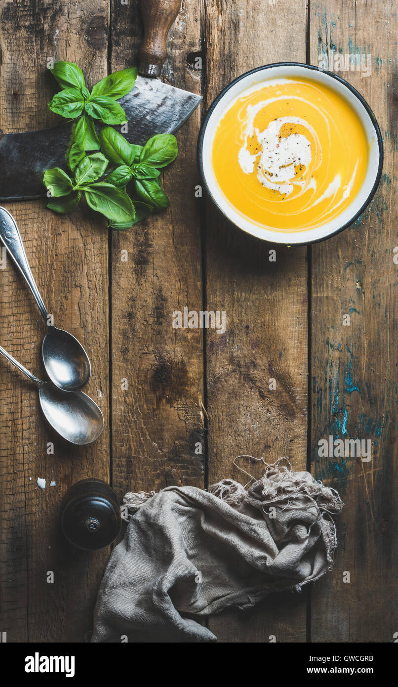 Pumpkin cream soup in bowl with fresh basil and spices over old rustic wooden background, top view, copy space, vertical composi Stock Photo