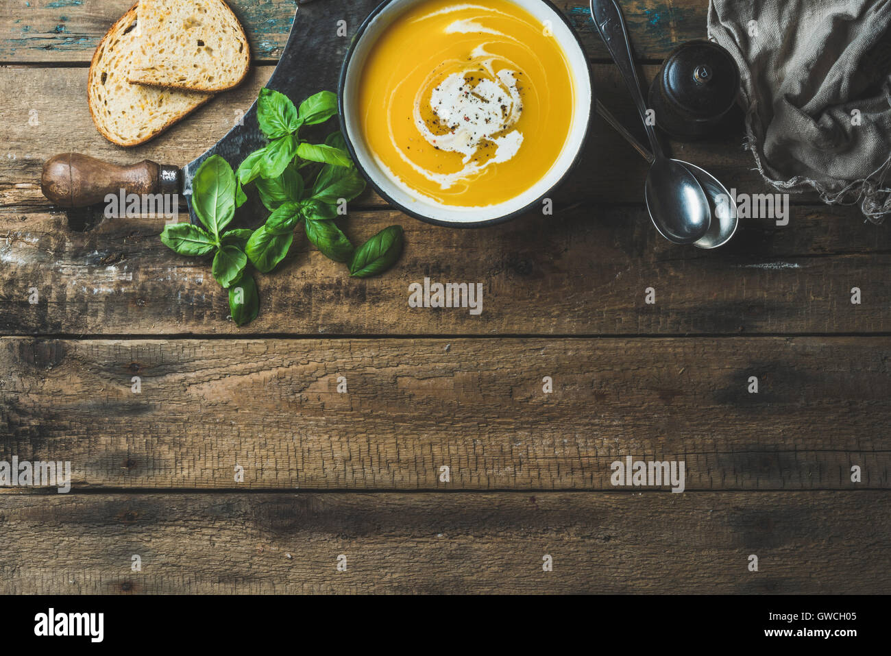 Pumpkin cream soup in bowl with fresh basil, spices and grilled bread slices over old rustic wooden background, top view, copy s Stock Photo