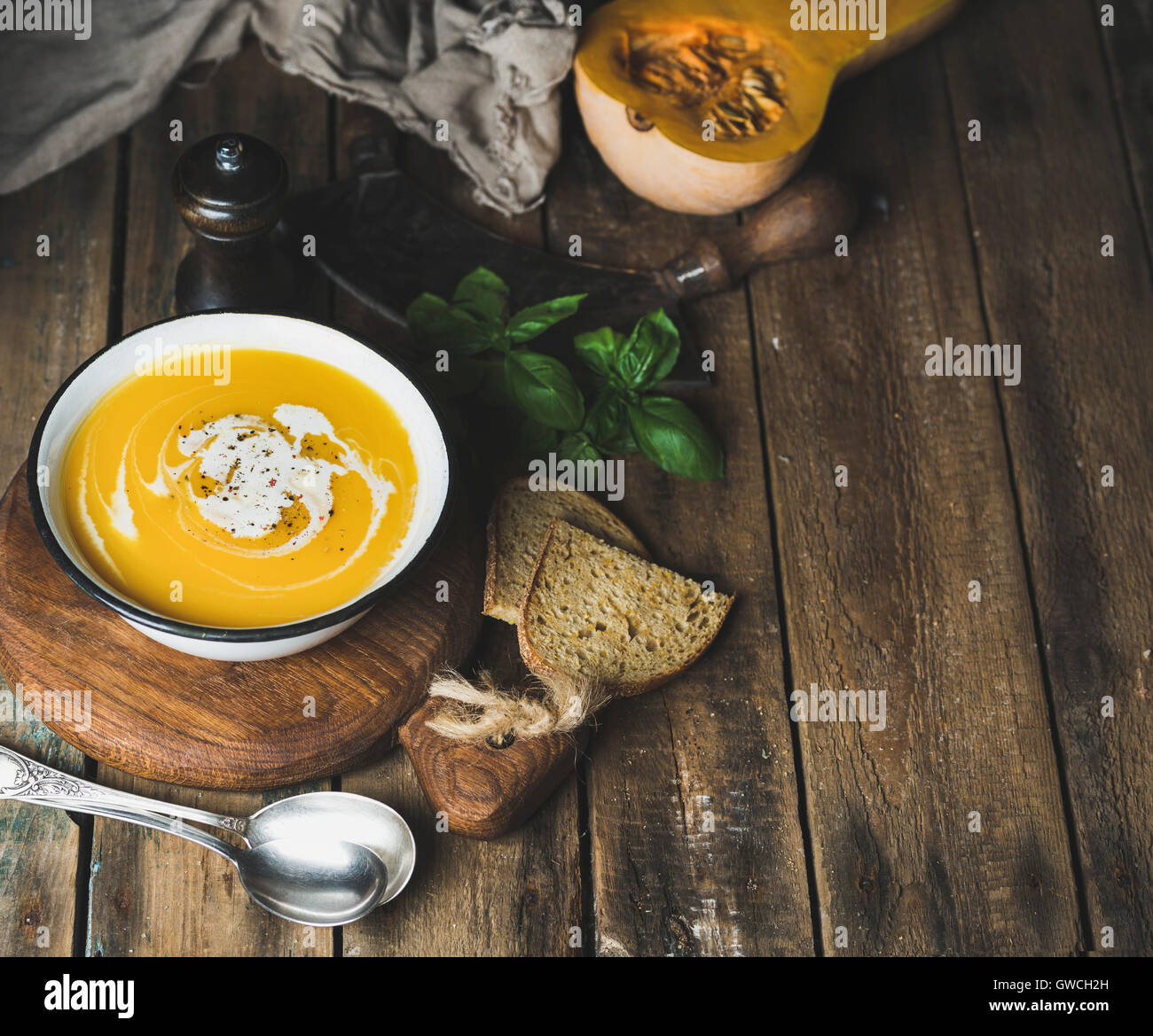 Pumpkin cream soup in bowl with basil leaves, spices and grilled bread slices served with fresh pumpkin over old rustic wooden b Stock Photo