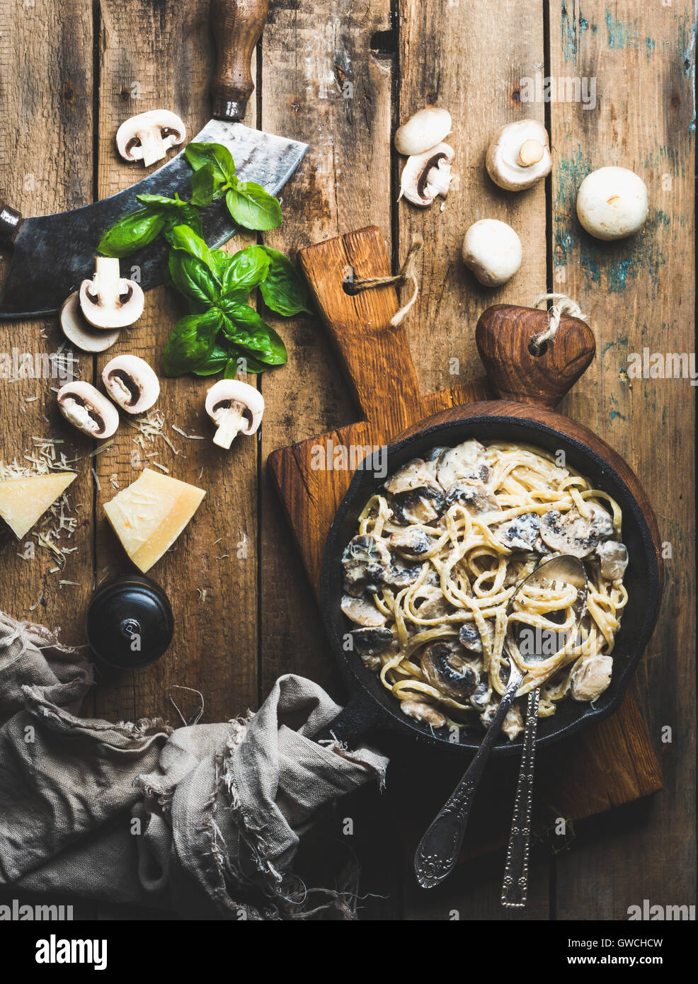Italian style dinner. Creamy mushroom pasta spaghetti in cast iron pan on wooden boards with Parmesan cheese, fresh basil leaves Stock Photo