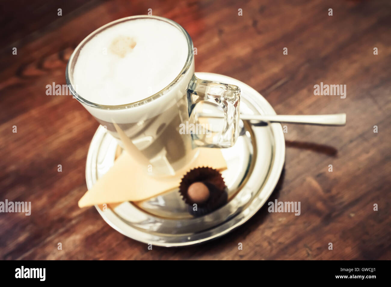 Glass mug full of Cappuccino stands on wooden table in cafeteria. Closeup photo with soft selective focus Stock Photo