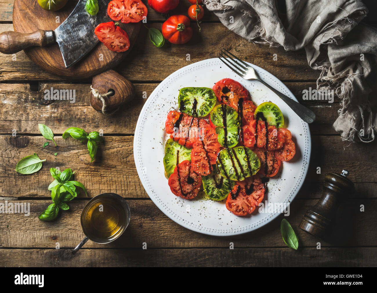 Heirloom tomato salad with olive oil, balsamic vinegar and basil over old rustic wooden background, top view, horizontal composi Stock Photo