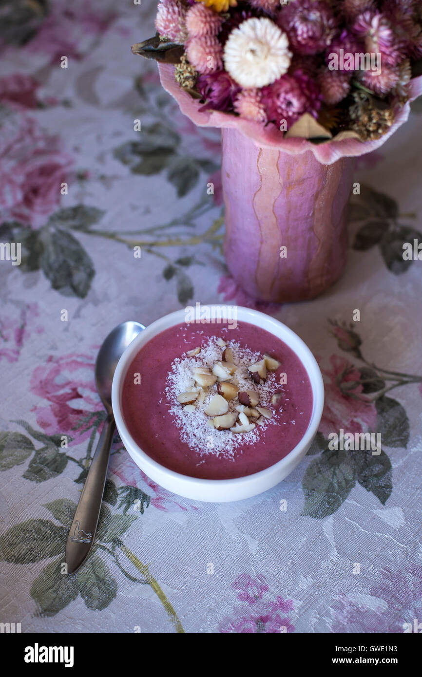 Raspberry smoothie bowl topped with coconut and chopped Brazil nuts on