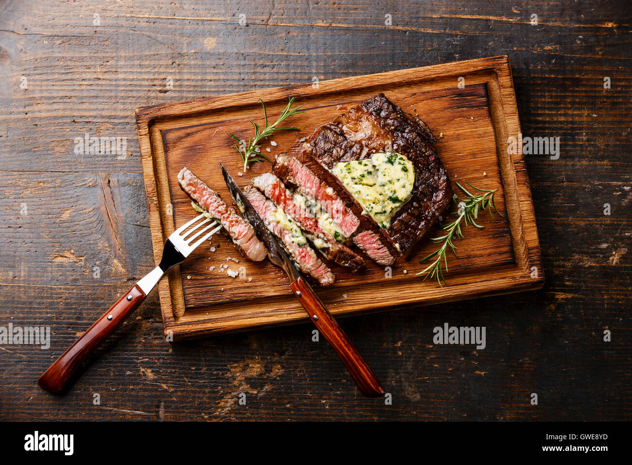 Sliced grilled Medium rare steak Ribeye with herb butter on cutting board on wooden background Stock Photo