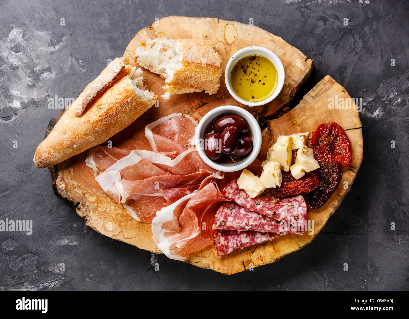 Cold meat plate with prosciutto, salami, bread and olives on wooden board on gray concrete stone background Stock Photo