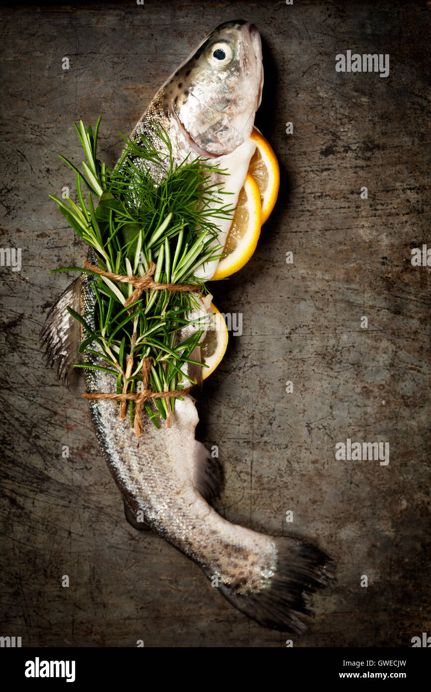 Raw rainbow trout with lemon, herbs and spice on rustic background