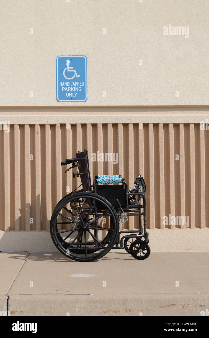 Wheelchair parked in font of handicapped parking sign Stock Photo