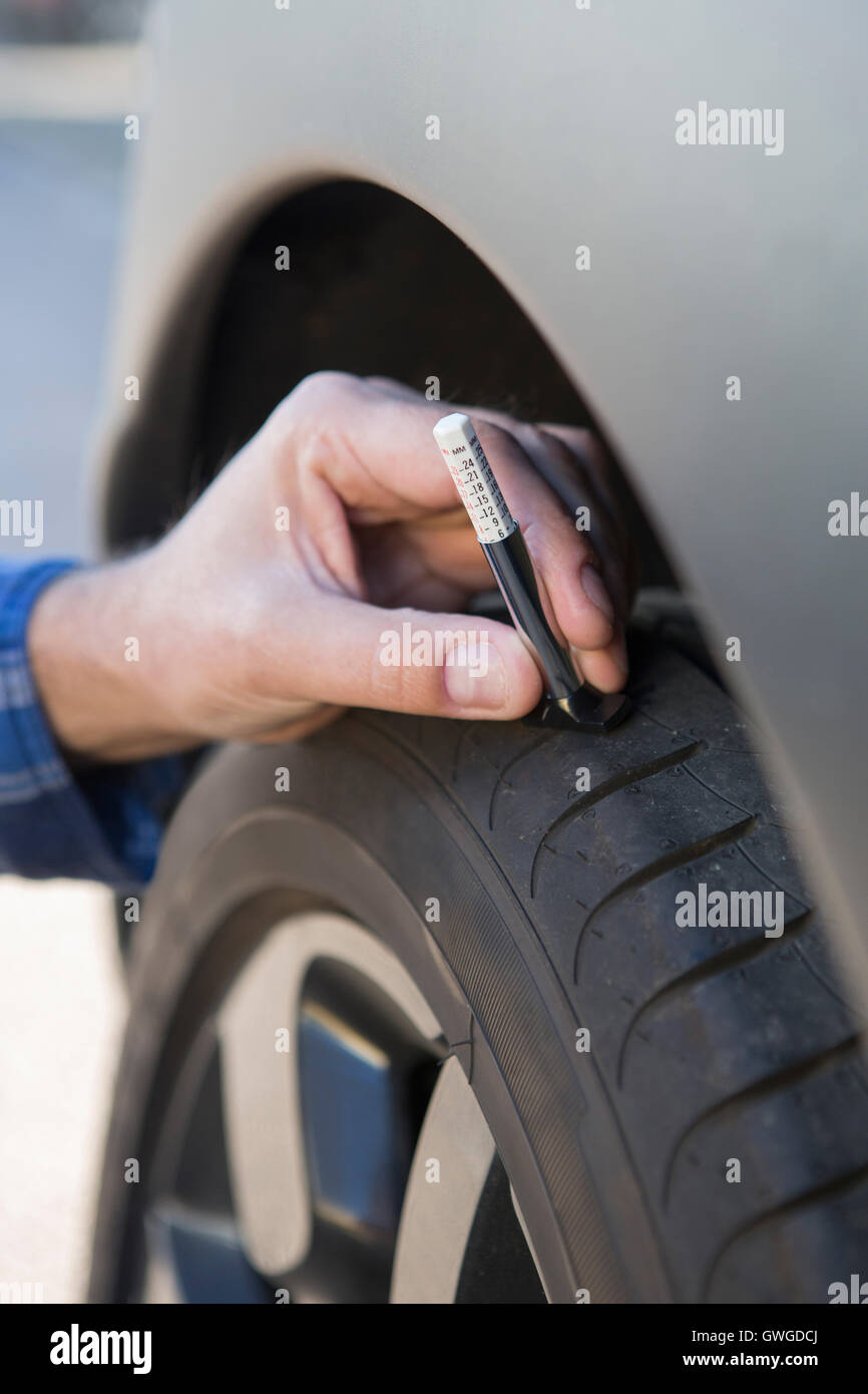 Close-Up Of Man Checking Tread On Car Tyre With Gauge Stock Photo