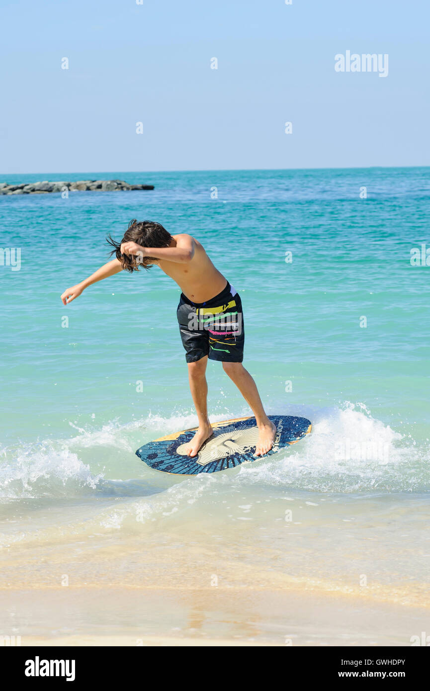 Teen (young boy) surfing with his skim board at the beach, Dubai Stock