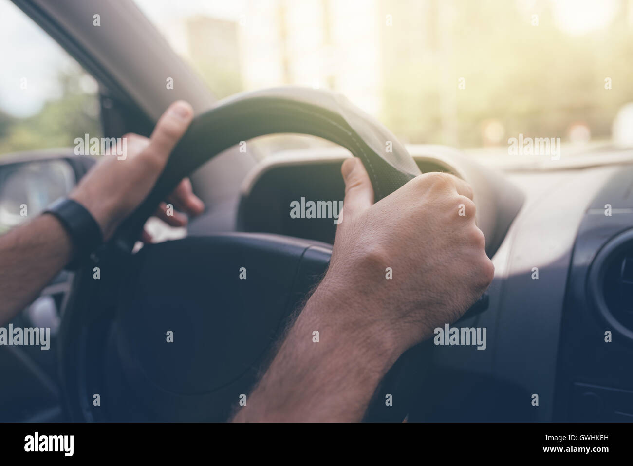 Driving through the city streets, close up of male hands holding vehicle steering wheel, selective focus Stock Photo