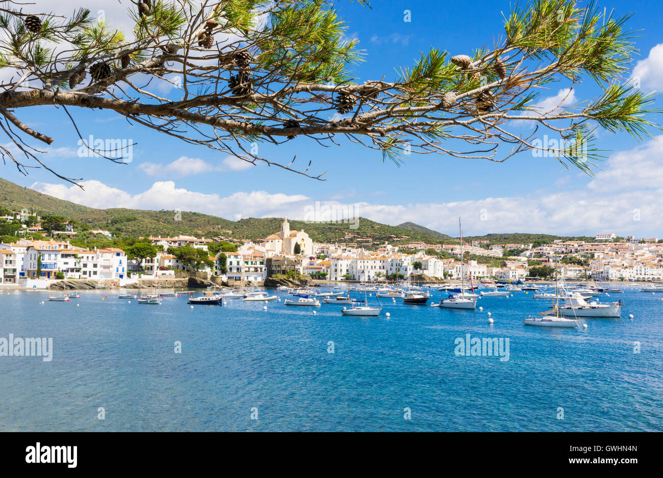 Whitewashed village of Cadaques topped by the Church of Santa Maria overlooking boats in the blue waters of Cadaques Bay, Spain Stock Photo