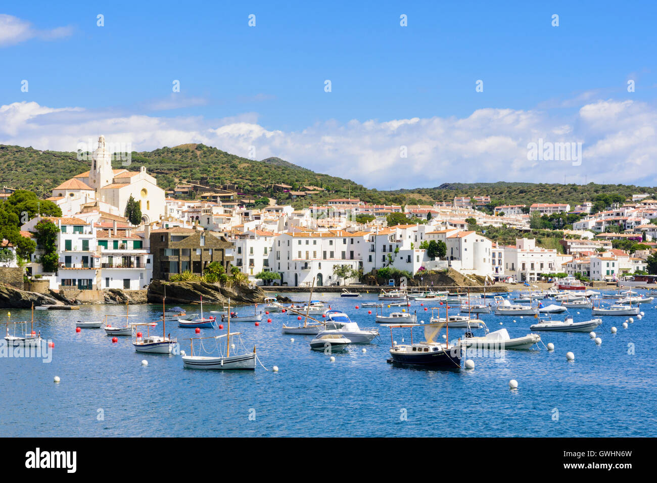 Whitewashed Cadaques town topped by the Church of Santa Maria overlooking boats in the blue waters of Cadaques Bay, Spain Stock Photo