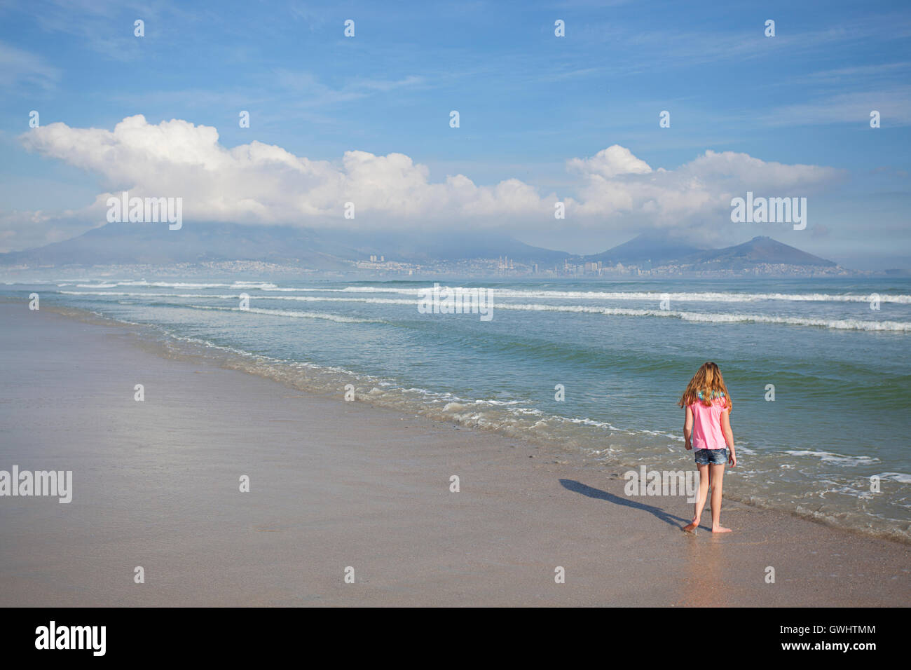 Young girl standing on the beach with Table Mountain in the background, Milnerton Beach, Western Cape, South Africa Stock Photo