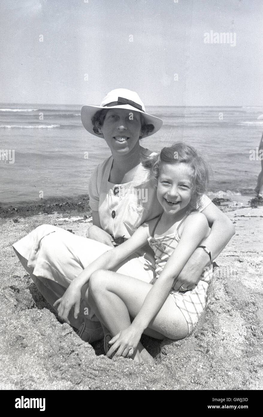 1938, historical, mother sitting with happy daughter on a sandy beach ...