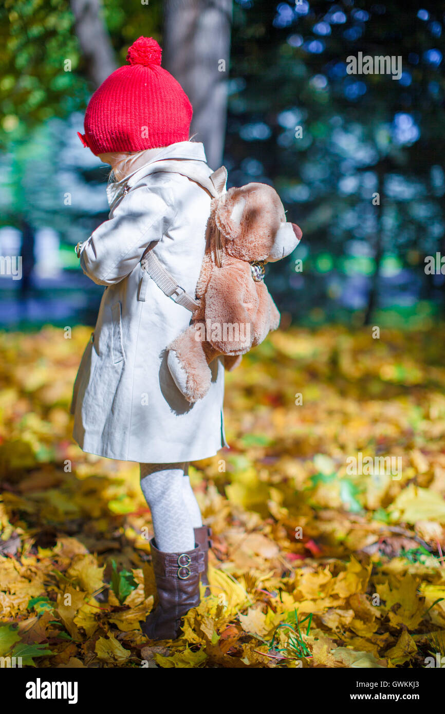 Little cute girl with a backpack-bear walks in the autumn forest on beautiful sunny day Stock Photo