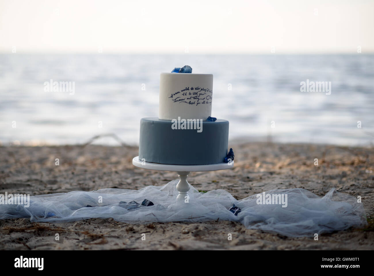 Blue two-tiered wedding cake on a sandy beach, decorated with blue stones. Wedding cake on the sand at sunset Stock Photo