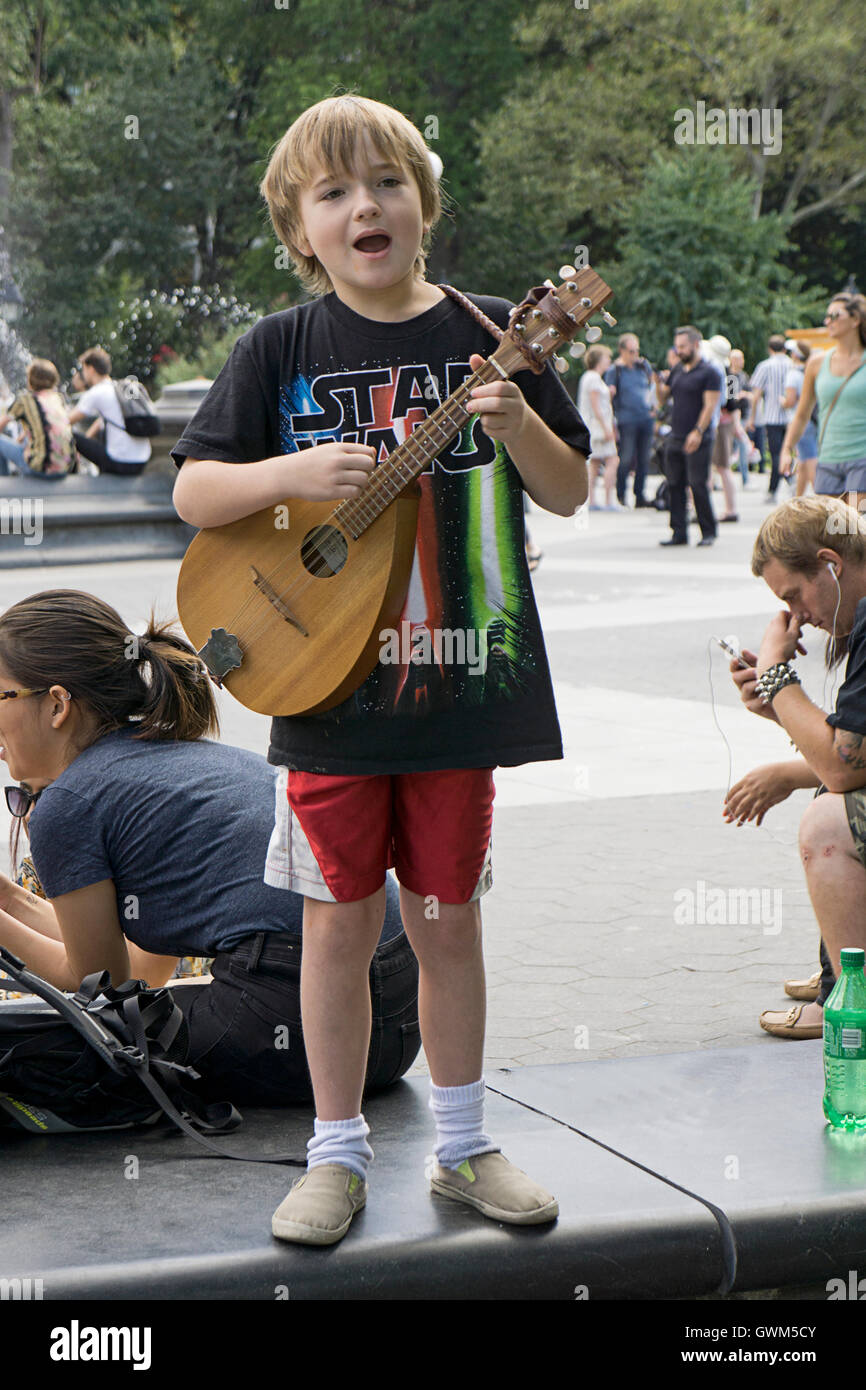 Under parental supervision, a 9 year old boy playing the guitar for tips in Washington Square Park in Greenwich Village, NYC Stock Photo