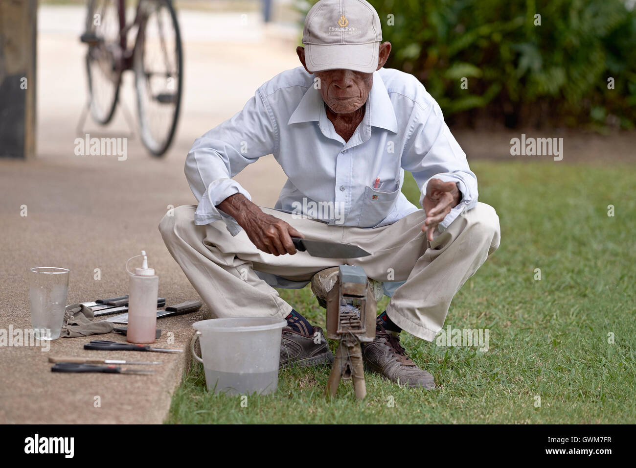 Knife grinder. 75 year old elderly man at work sharpening household implements . Thailand S. E. Asia Stock Photo