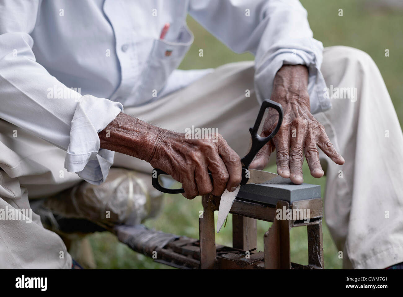 Knife grinder sharpening a pair of scissors. Hands of an elderly Asian man at work. Thailand Southeast Asia Stock Photo