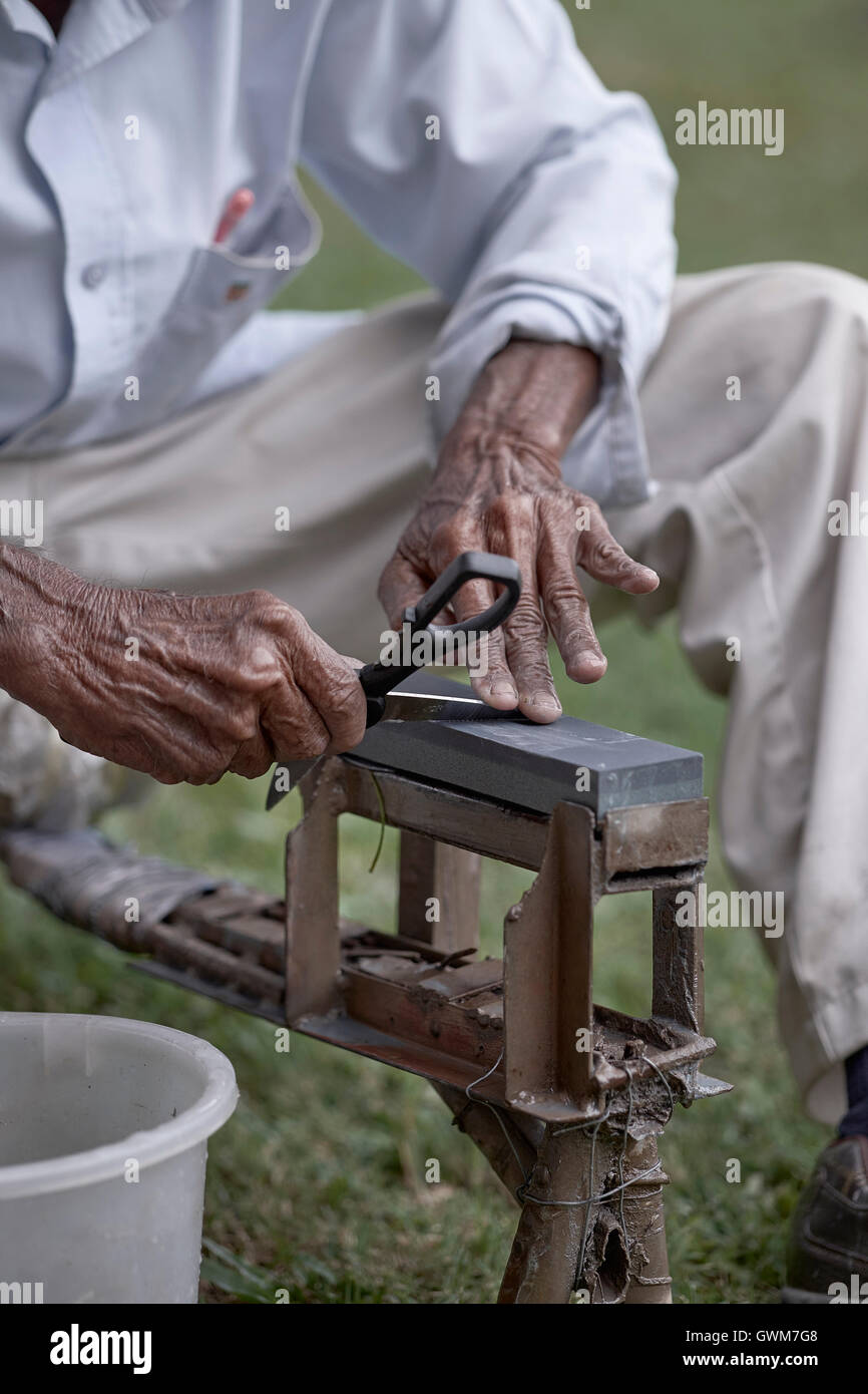 Knife grinder sharpening a pair of scissors. Hands of an elderly Asian man at work. Thailand Southeast Asia Stock Photo