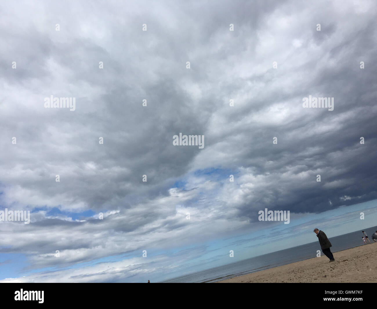Man on beach, with lots of clouds in sky, in St Andrews, Fife, Scotland. Stock Photo