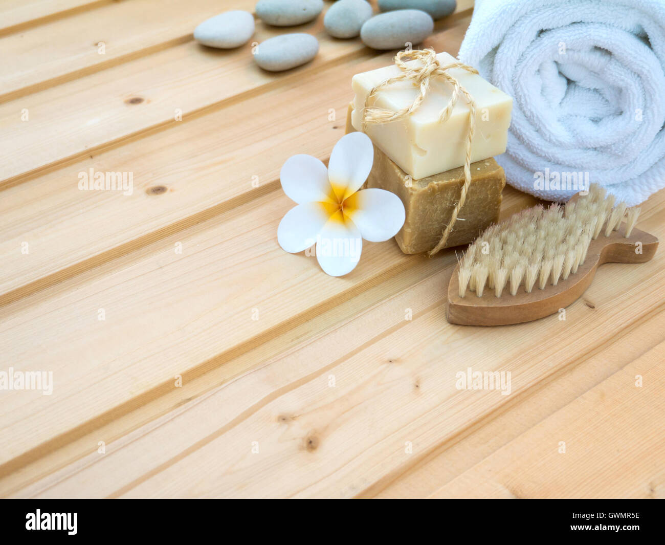 White rolled towel, tiare flower, soap tied with jute rope, stones and fish shaped nail brush on the wooden planks Stock Photo
