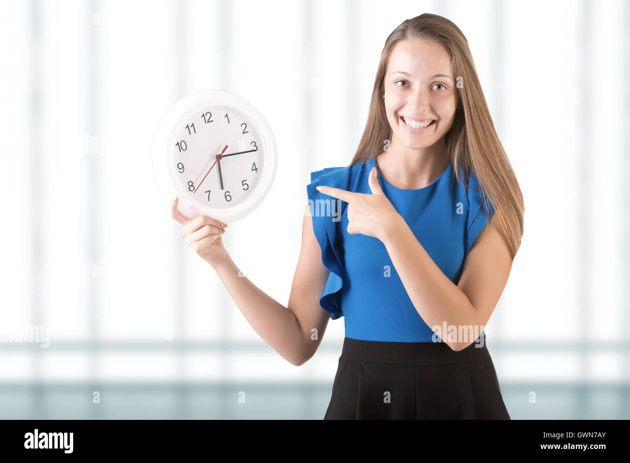 Young woman smiling and pointing at a clock. Isolated in white. Stock Photo