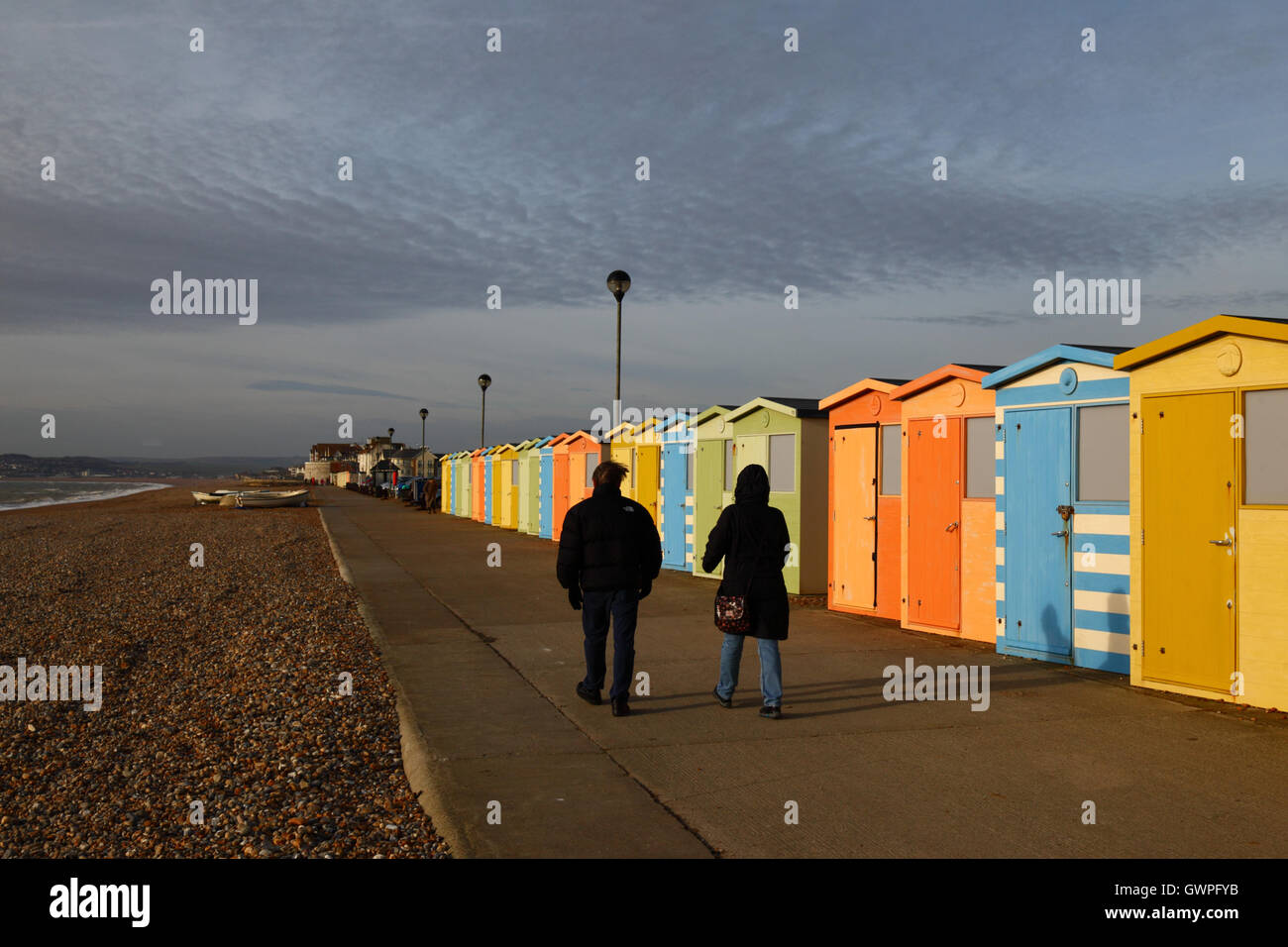People walking past line of wooden beach huts on sea front on a winter afternoon, Seaford, East Sussex, England Stock Photo
