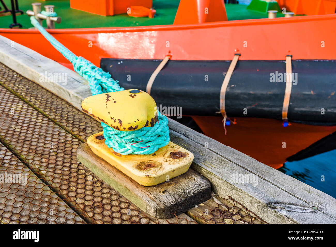 Yellow bollard with tight green rope to a red boat. Stock Photo