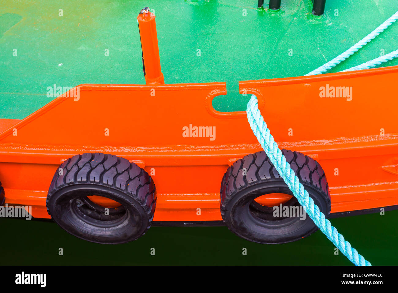 Red and green boat moored dockside. Car tires used as fenders and a green rope hang from the side. Stock Photo