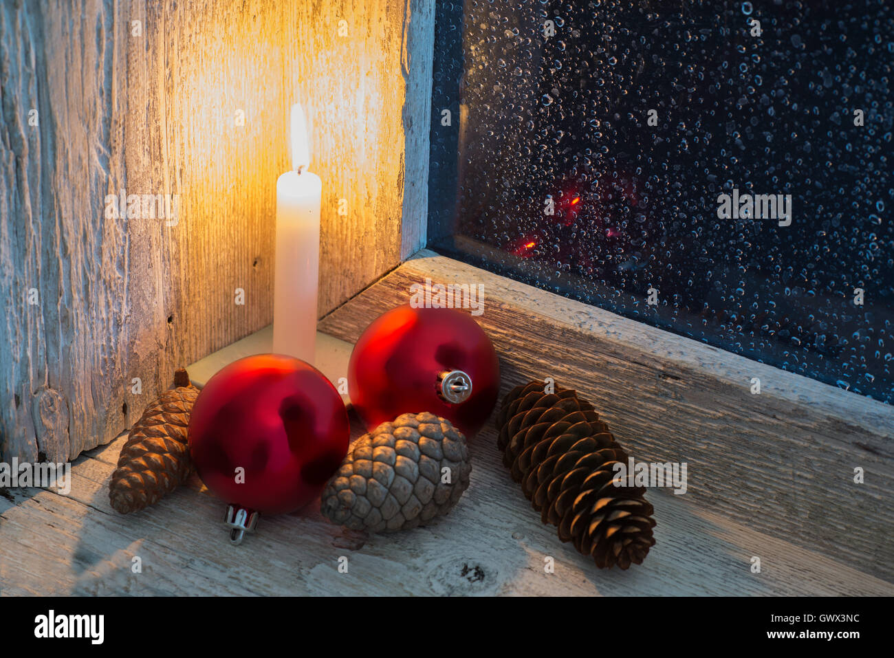 burning candle and Christmas ornaments in an old window with wet glass Stock Photo