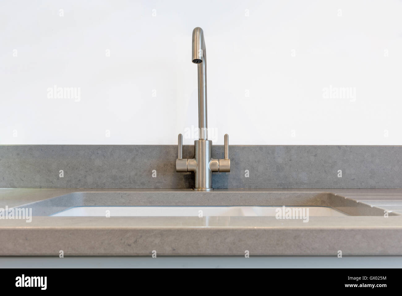 Brushed steel mixer tap with grey worktop and white kitchen sink Stock Photo