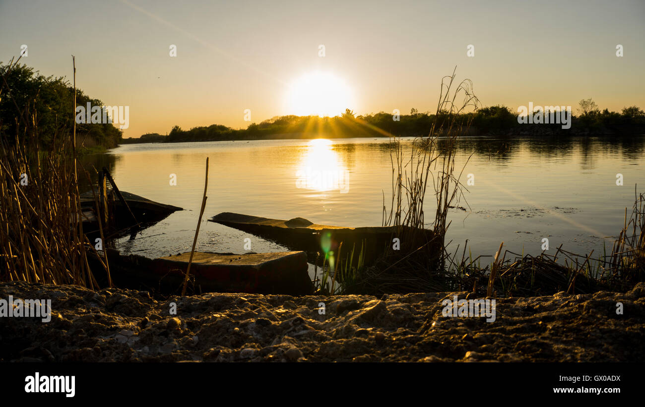 Sun setting over lake with sunken boat Stock Photo