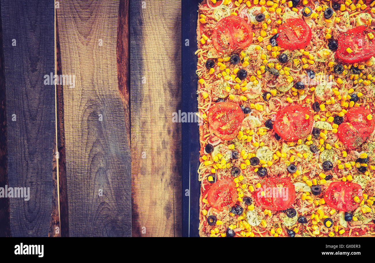 Vintage toned homemade tuna pizza with tomatoes, olives, onion and corn on wooden background, top view, space for text. Stock Photo