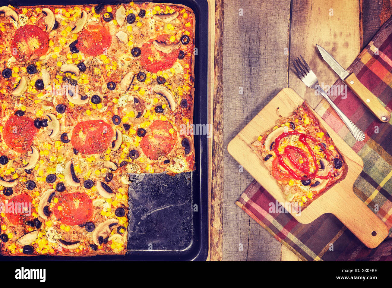 Vintage toned homemade tuna pizza with tomatoes, olives, onion and corn on wooden background, top view. Stock Photo