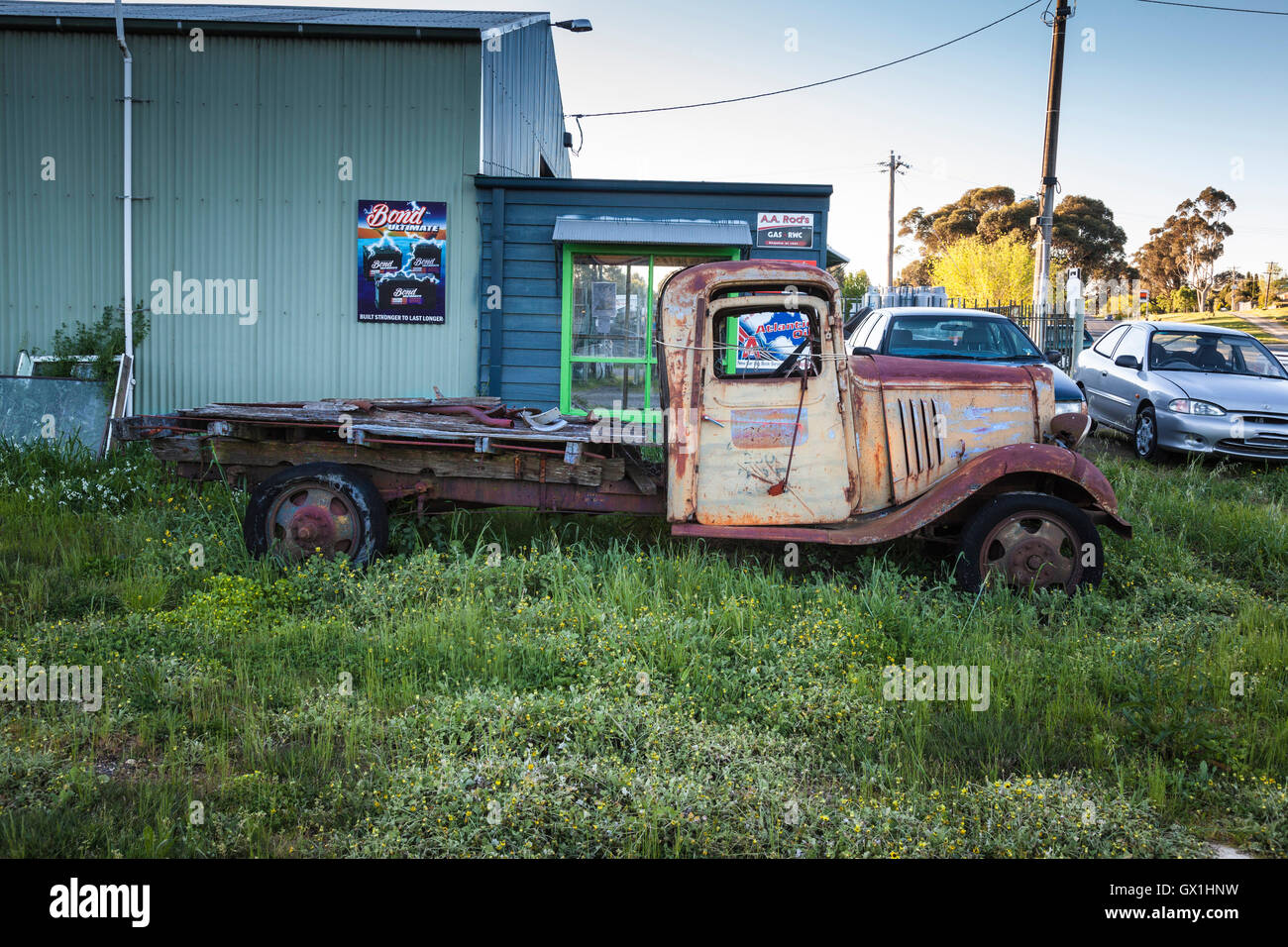 A rusty old truck, in tall grass, beside a second hand car yard Stock Photo